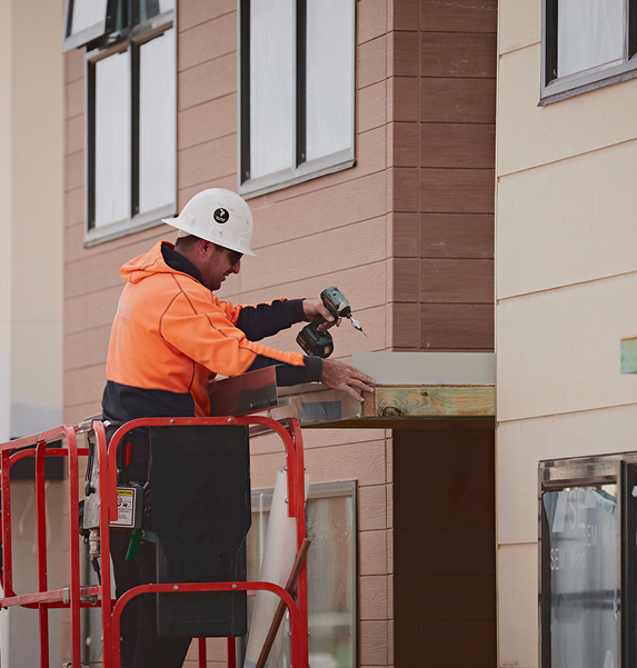 Construction worker installing exterior cladding on new residential building