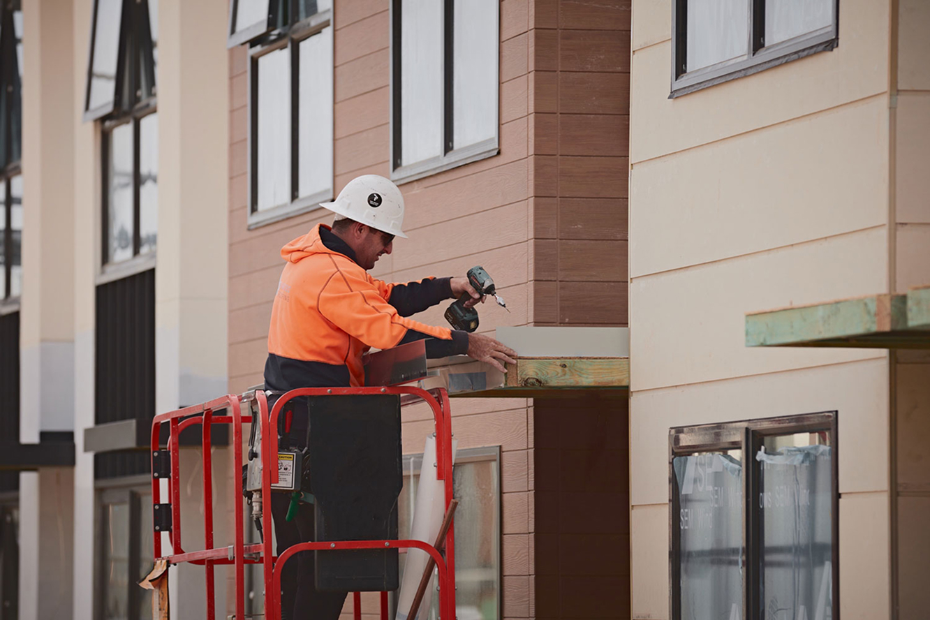 Construction worker installing exterior cladding on new residential building