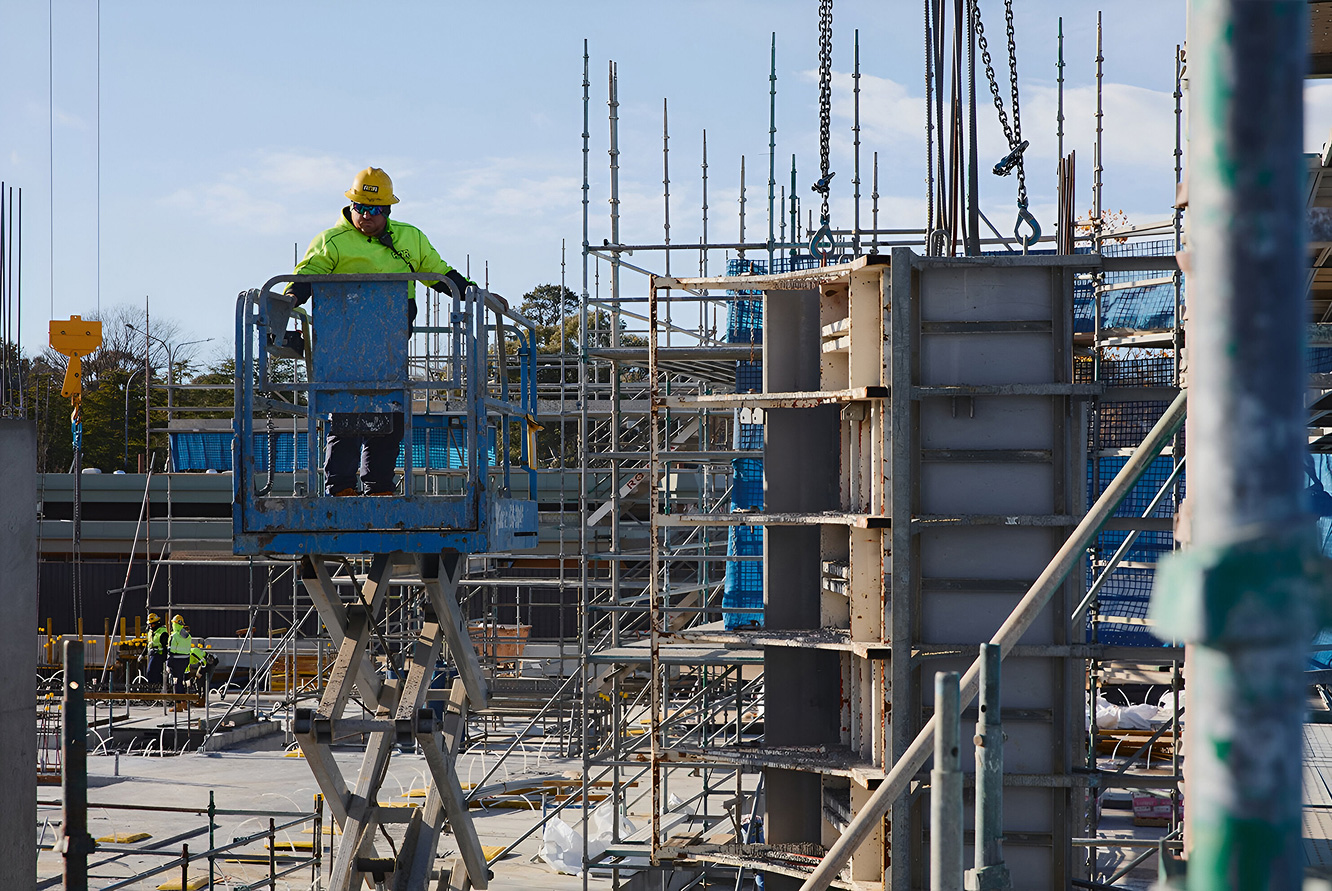 Worker using elevated lift among scaffolding at the Dickson Village development